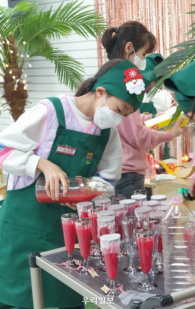 지역 농가에서 생산한 딸기로 만든 딸기우유, 크리스마스 건배용 음료로 만든 사과,당근,비트 착즙주스를 어린이가 주스잔에 따르고 있다.